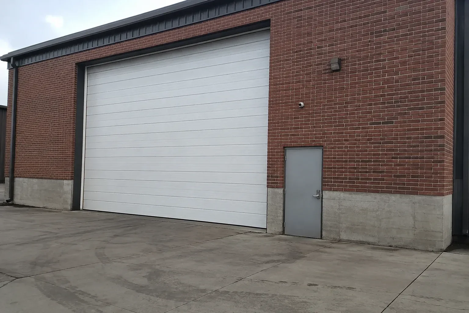 Tall closed sectional loading door beside a personnel door at a brick unit. — Commercial Sectional Door Repair, Oro-Medonte