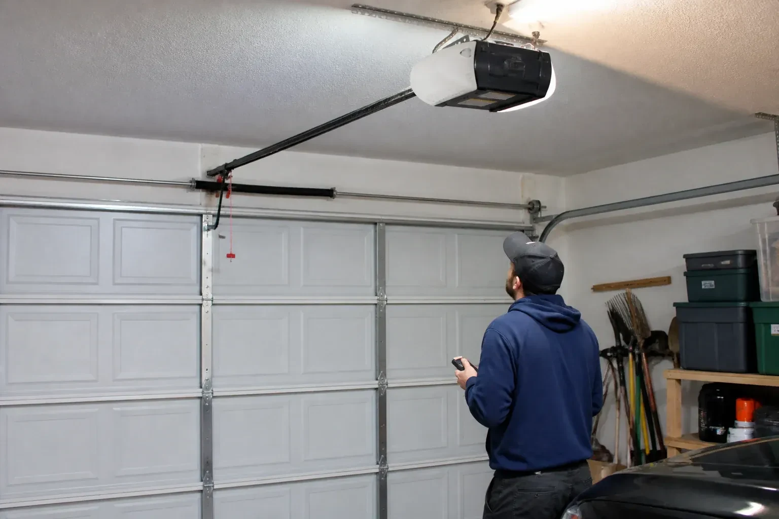 A person holding a remote looks toward an overhead garage-door opener and rail. — Garage Door Opener Diagnosis and Repair, Oro-Medonte