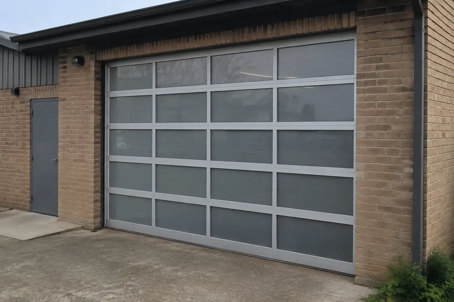 Closed glazed sectional door in a grey metal frame at a brick workshop. — Full-View Glass Garage Door Installation, Oro-Medonte